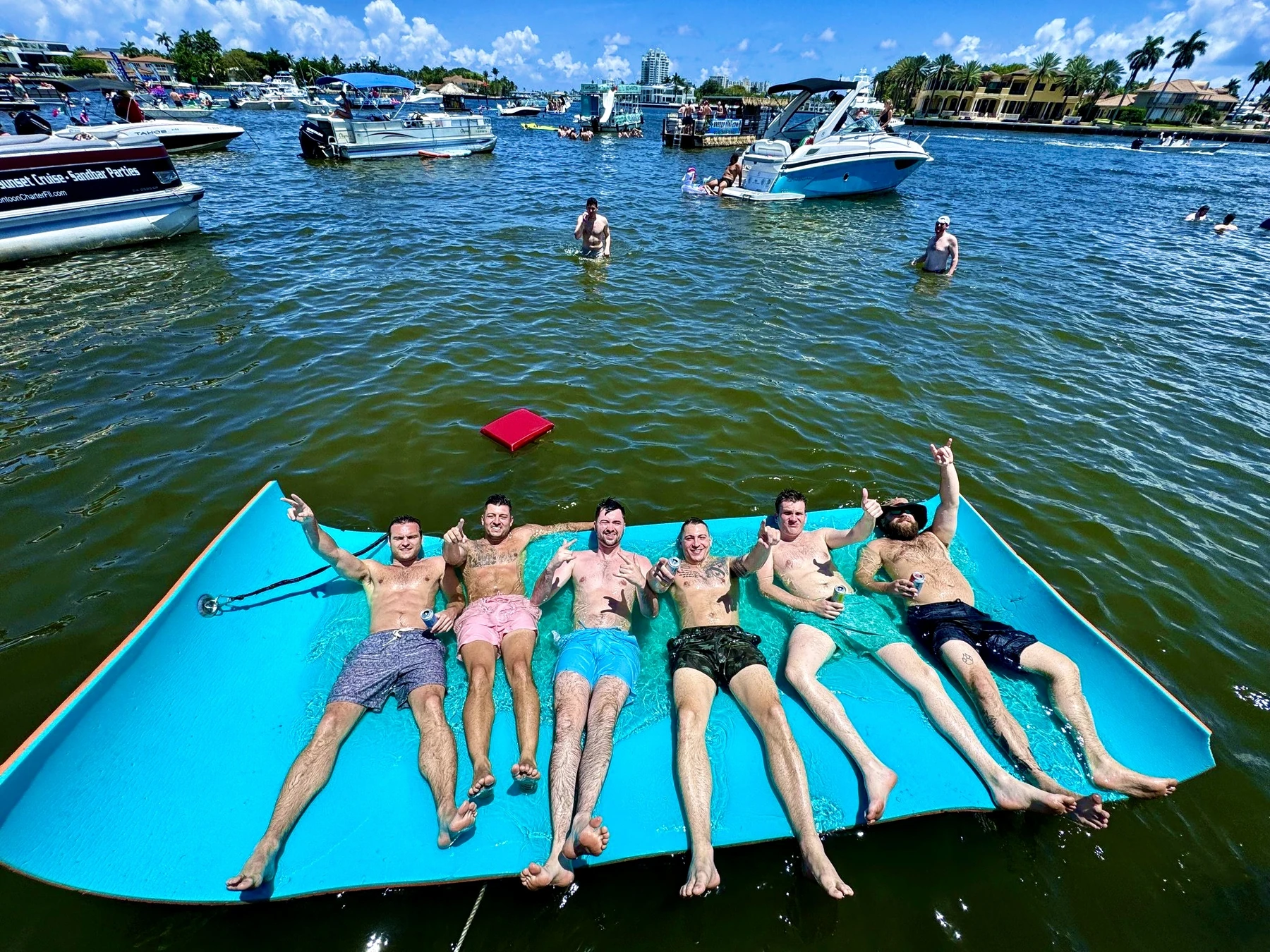 Six bachelor party friends lying side by side on Freaky Tiki's turquoise floating mat at the Fort Lauderdale sandbar